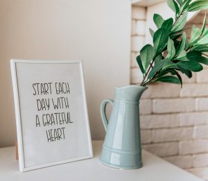 Framed quote 'Start each day with a grateful heart' next to a vase indoors.