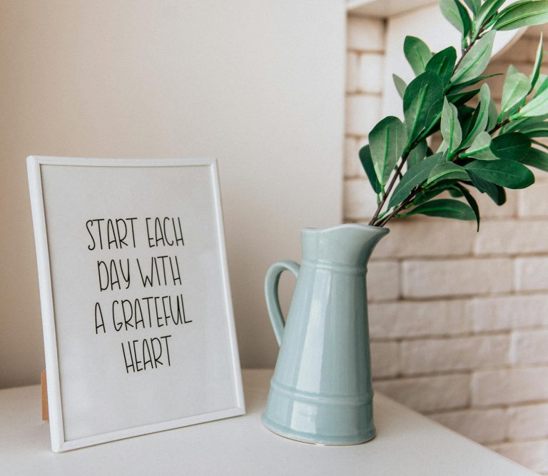 Framed quote 'Start each day with a grateful heart' next to a vase indoors.