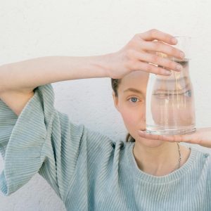 Woman holding a glass jug reflecting her face, creating a unique visual distortion.