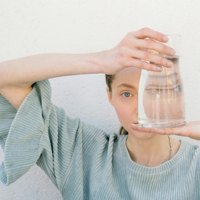 Woman holding a glass jug reflecting her face, creating a unique visual distortion.